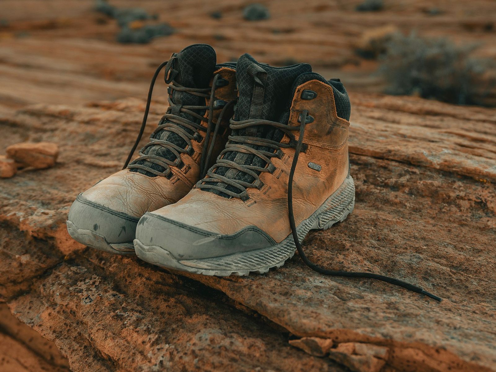 Een paar halfhoge wandelschoenen van lichtbruin leer met een grijze neus en losse veters, op rood zandsteen