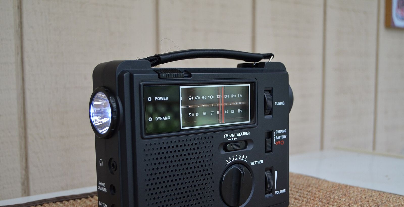 Zwarte draagbare radio met handvat, met een brandend lampje aan de zijkant, een schaal voor AM en FM en een schakelaar met de standen dynamo en battery